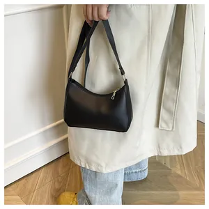 Detail of a minimalist black leather crescent shoulder bag with adjustable strap and gold zip