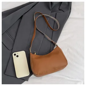 Detail of a brown leather crescent shoulder bag shown next to a smartphone for size reference