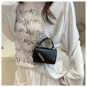 Detail of black patent leather crossbody bag with gold metal trim and chain strap