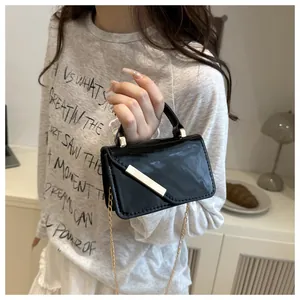 Close-up of black patent leather mini crossbody bag with gold metal bar and chain strap