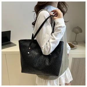 Close-up of black woven large tote bag with textured pattern and gold rivet shoulder strap