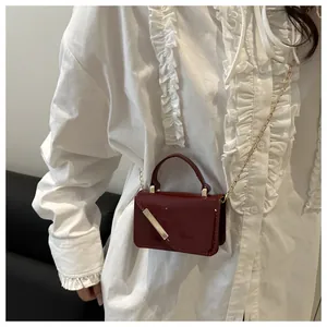Close-up of burgundy patent leather crossbody bag with chic gold metal bar and chain strap