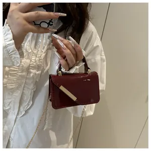 Detail of burgundy patent leather mini square bag with gold metal bar and chain strap