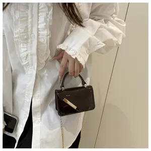 Detailed close-up of dark glossy patent leather bag with modern gold metal trim and chain