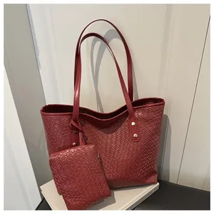 Close-up of burgundy woven leather tote bag texture with matching pouch and gold rivets