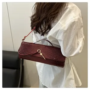 Détail du sac à main bordeaux à motif crocodile et fermoir doré porté par un mannequin