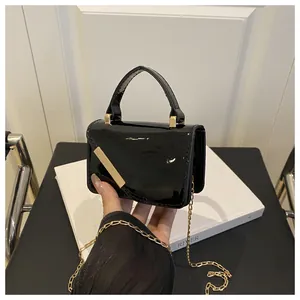 Detailed close-up of glossy black patent leather mini bag with gold chain strap and buckle