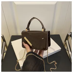 Close-up of brown patent leather mini bag with gold bar detail and elegant chain strap