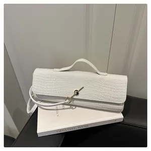 Détail du sac baguette blanc à motif crocodile avec boucle en métal doré sur livres
