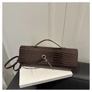 Détail de la texture crocodile marron foncé et de la boucle hexagonale dorée sur le sac