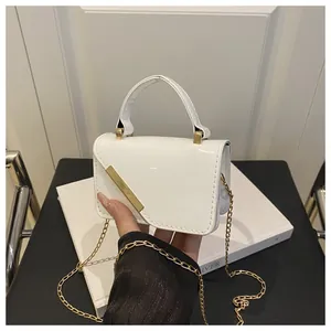 Detail of white glossy patent leather handbag with gold metal trim and chain strap