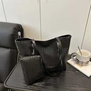 Large black woven tote bag with matching pouch and slim shoulder straps on a desk