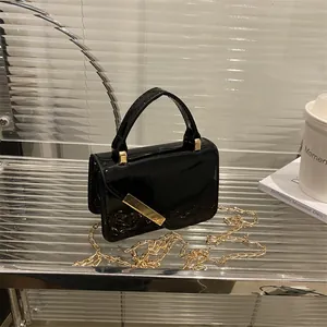 Minimalist black patent leather crossbody bag with gold chain strap on display
