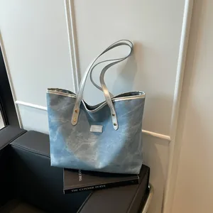 Light blue denim tote bag with silver handles and fashion tag on a minimalist background