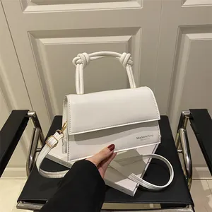 Minimalistische weiße quadratische Klapptasche mit gedrehtem Griff und goldenen Schnallen