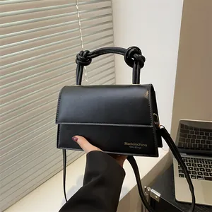 Minimalistische schwarze Schultertasche mit Knotengriff und Goldaufdruck im Büro-Szenario