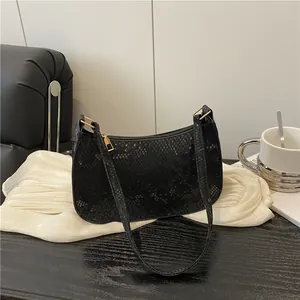 Chic black snakeskin embossed underarm bag with gold zipper on a dark wooden surface