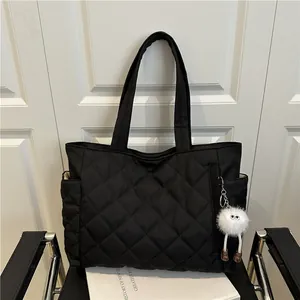 Minimalist black quilted tote bag with diamond stitching and plush pendant on a chair