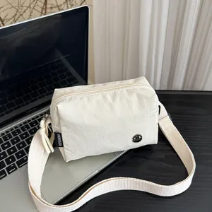 Borsa a tracolla minimalista in nylon bianco avorio con tracolla larga su scrivania