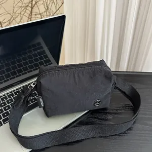 Borsa a tracolla minimalista in nylon nero con tracolla regolabile su un laptop