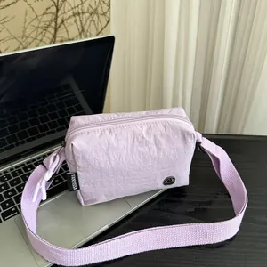Borsa a tracolla quadrata in nylon plissettato lilla con tracolla in tessuto su laptop