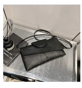 Dettaglio pochette a busta nera con trama coccodrillo e manico rotondo raffinato