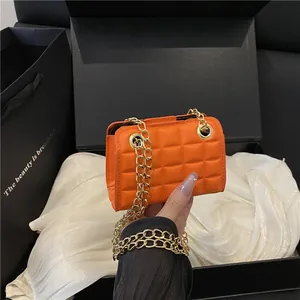 Bright orange quilted crossbody bag with gold chain strap on black gift box display