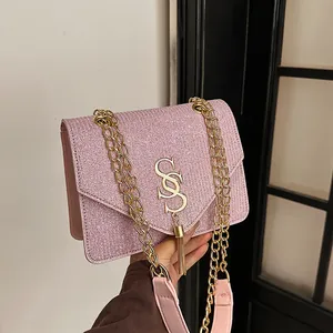 Pink sequin crossbody bag with gold metal tassel and chain strap in hand