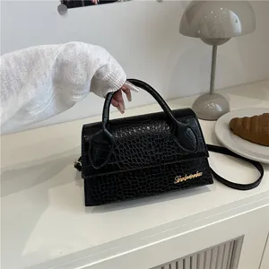 Elegant black crocodile pattern crossbody bag with gold logo on a white table