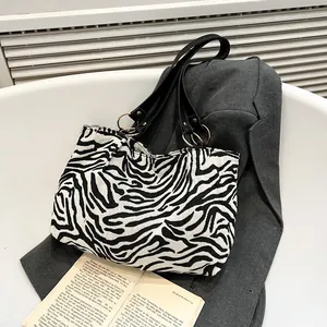 Fashionable zebra print tote bag with black leather handles and gold rings on grey blazer