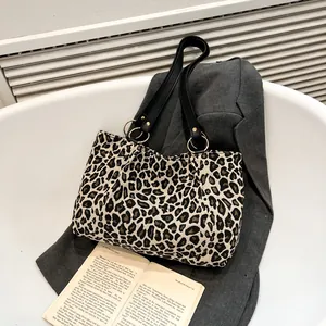 Chic leopard print canvas tote bag with black leather straps on a grey blazer background