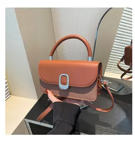 Detail of a brown leather handbag featuring a woven texture and round metal buckle