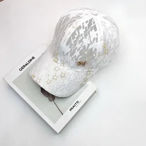 Detail of white lace baseball cap with floral embroidery and golden crystal M metal logo