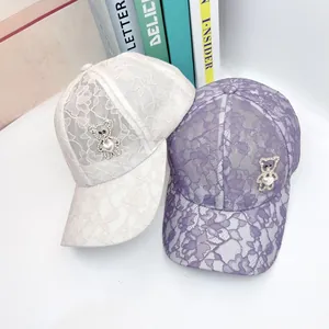 Détail d'une casquette en dentelle avec un ours en strass et une perle en forme de cœur