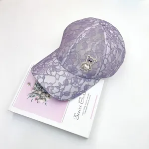 Détail d'une casquette en dentelle violette avec ours en strass et perle de cœur