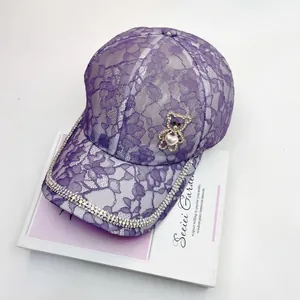 Détail de casquette en dentelle violette avec bord strass et ornement d'ours perlé