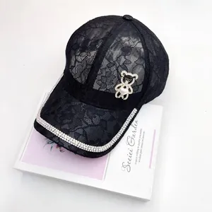Détail d'une casquette en dentelle avec ours en strass et perle en forme de coeur