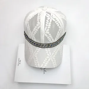Close-up of white floral lace baseball cap with sparkling blue rhinestone and silver bead trim