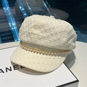 Détail d'une casquette gavroche en tweed beige avec chaînes et perles de fantaisie