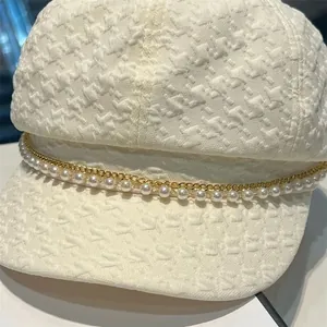 Détail de la casquette blanche avec texture pied-de-poule, chaîne dorée et perles