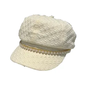 Casquette gavroche beige avec chaîne dorée perlée et texture pied-de-poule sur blanc