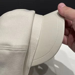 Detail of cream white newsboy hat showing wool-like fabric texture and faux leather brim