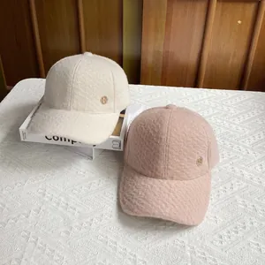 Close-up of wool baseball caps with golden H logo detail in beige and pink colors