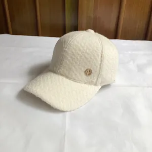 Detail of white sherpa fleece baseball cap featuring a golden metallic H logo emblem