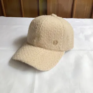 Close-up of beige fleece baseball cap featuring a round gold H logo metal detail