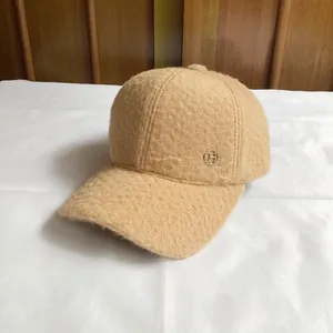 Detail of wool baseball cap featuring golden H letter logo and plush camel texture
