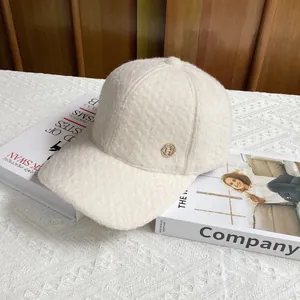 Close-up of cream wool baseball cap with golden H metal logo on textured lambskin fabric