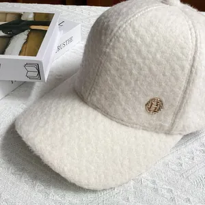 Close-up of off-white sherpa baseball cap featuring a gold H logo with crystal embellishments