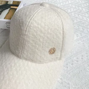 Detailed macro view of plush beige wool fabric and H-logo rhinestone metal badge on cap