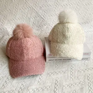 Close-up of plush faux fur pom-poms on pink and cream lamb wool baseball caps